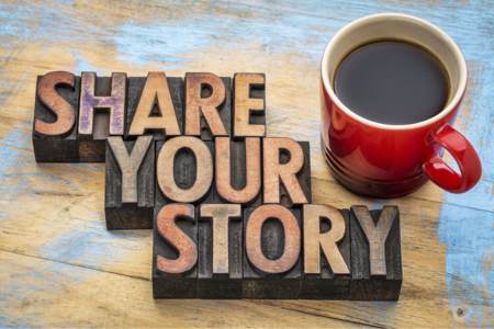 Sign that says "Share Your Story" next to a cup of coffee