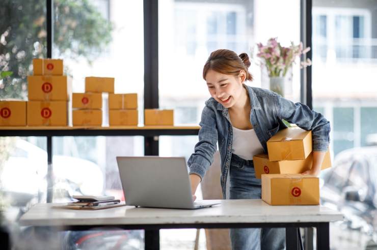 eCommerce store owner smiling while using the laptop and holding boxes