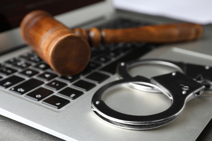 A gavel and handcuffs resting on top of a laptop