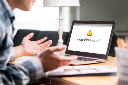 Man at desk with laptop computer displaying "page not found".
