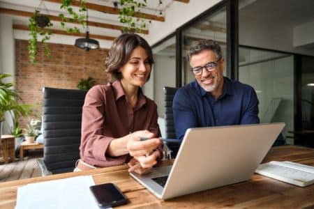man and woman sitting at a desk looking at a laptop
