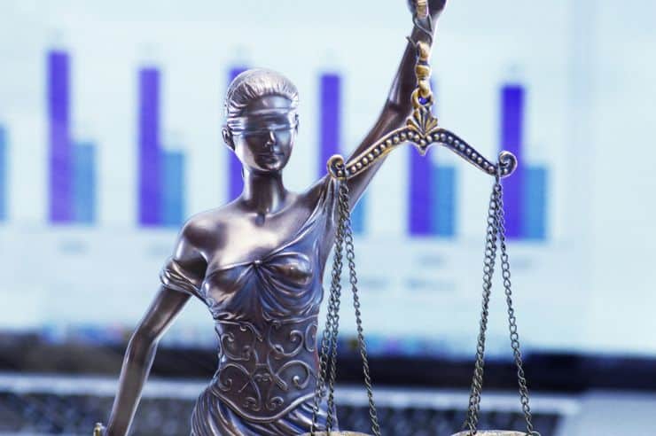 Scales of justice statue in front of marketing stats on a computer screen.