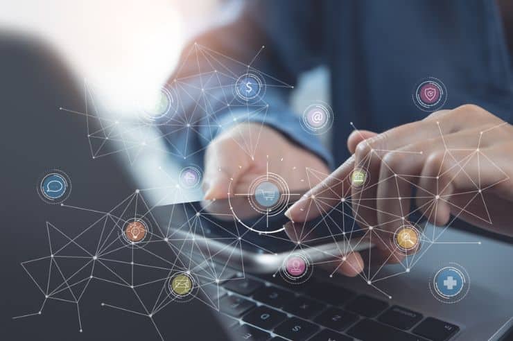 Hands using a smartphone and laptop with digital network icons overlay.